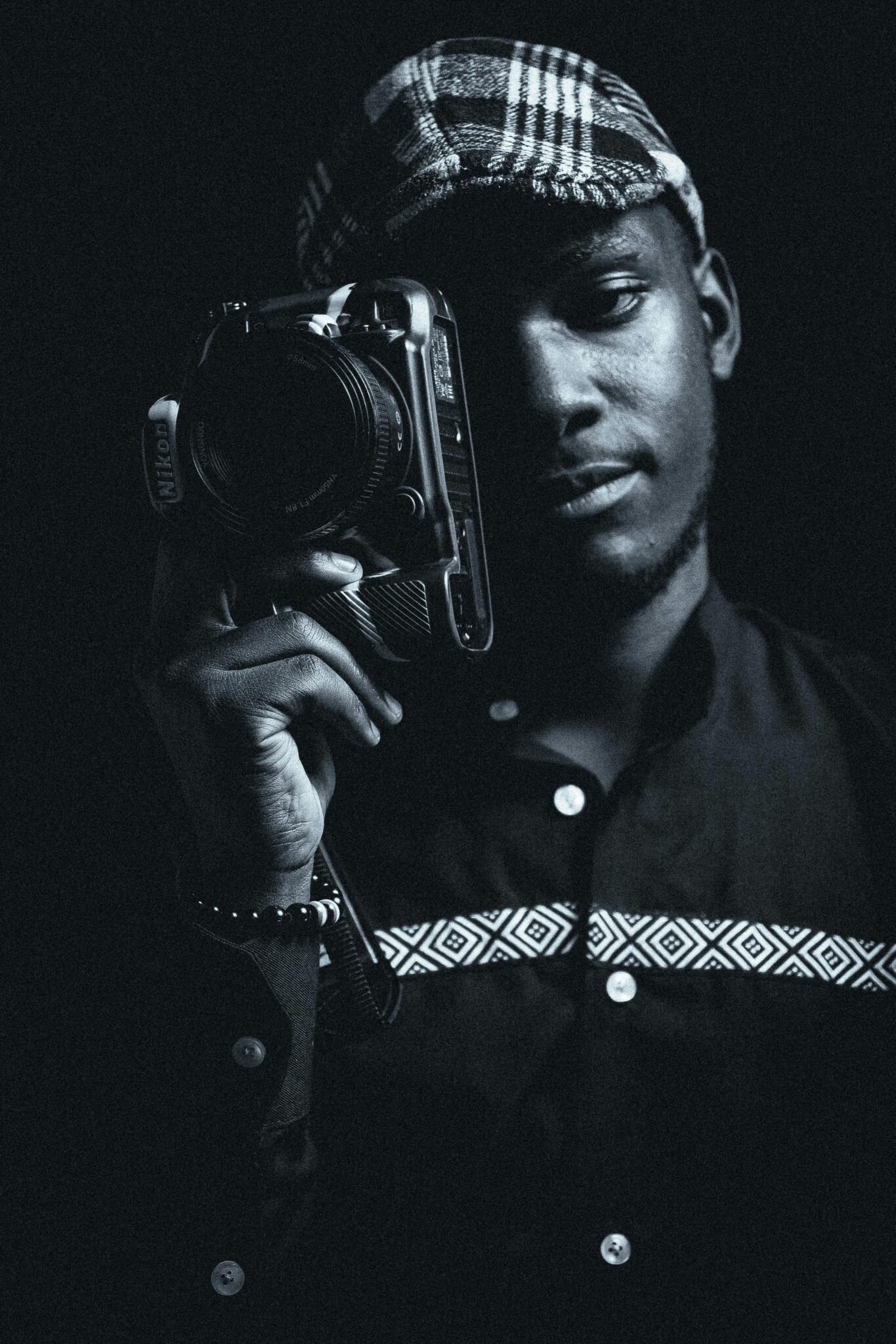 Black and white portrait of a stylish man holding a camera in a studio setting.